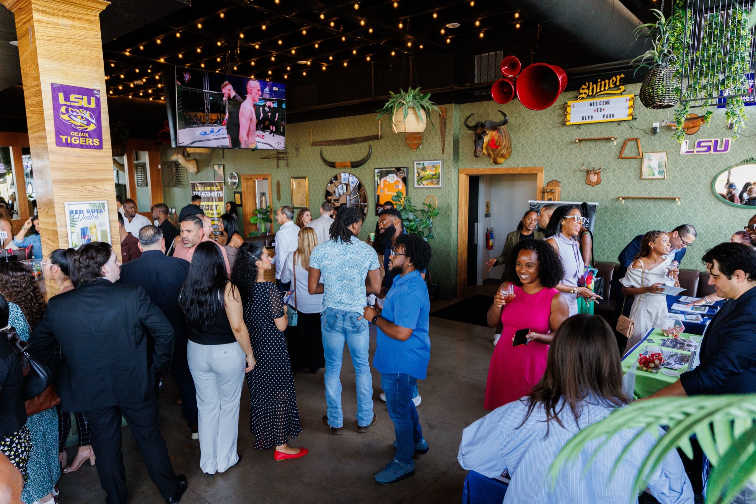 A full room of guests talking and laughing under string lights at a Builders, Brokers & Business social at BLVD Place in Houston.