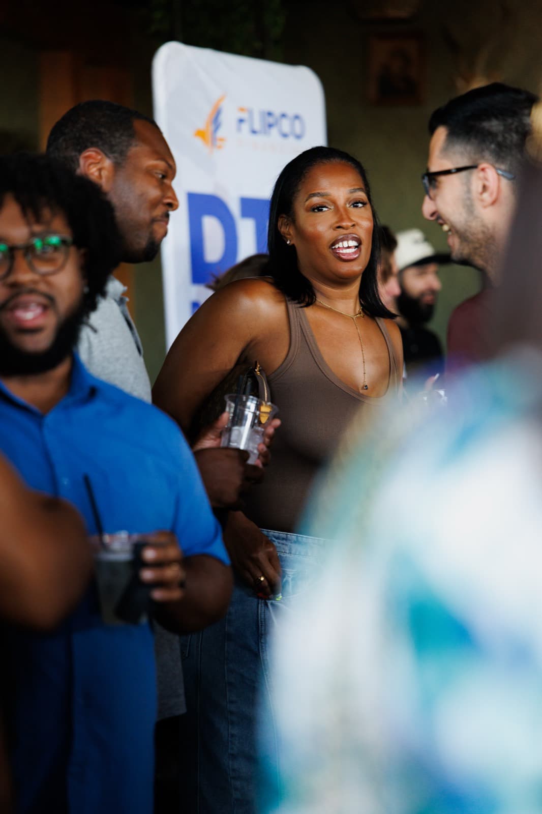 Guests laughing together in front of a sponsor banner at a Madu Rooms event.